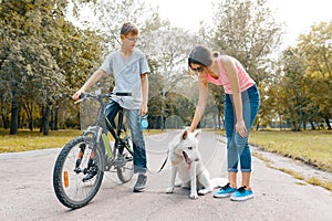 Children teenagers on the road in the park with white dog Husky with bike talking, smiling