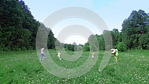 Children together with their mothers are playing with the ball on the chamomile meadow, near the forest. They have fun