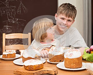 Children with traditional Easter homemade cakes and colored eggs. Teen boy and little girl sitting at the table full of