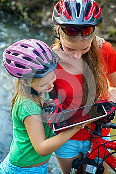 Children traveling bicycle in summer park. Bicyclist watch on tablet computer.