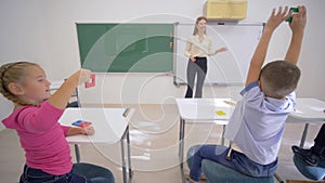 Children tuition, merry educator woman near board conducts cognitive lesson for cute pupils at desk in classroom of