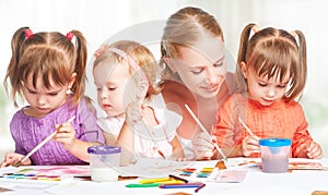 Children twin sisters draw paints with her mother in kindergarten