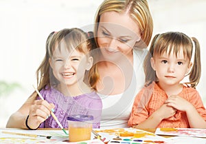 Children twin sisters draw paints with her mother in kindergarten on a white background