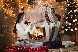 Children under Christmas tree at home celebrate winter holidays, they are having fun with fake snow