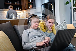 Children using laptop computer while mother is working in the kitchen. Protecting childs privacy online - concept.