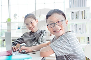 Children using notebook computer at library and smiling at camera,education and technology concept