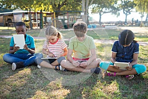 Children using tablet computer while sitting on grassy field