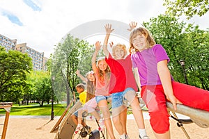 Children waive hands sitting in row on round bar