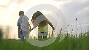children walking a in the park. boy and girl are holding hands walking on the grass in the park at sunset. happy family