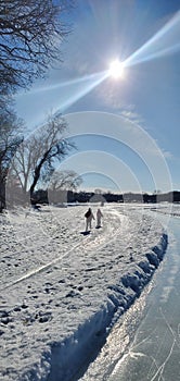 Children walking on a path on a snowy day over a frozen lake in the sunshine.