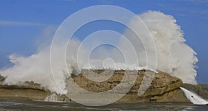 Children watching large wave crashing over rock