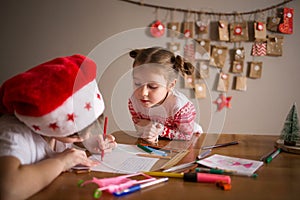 Children write letter to Santa Claus at home. sisters girls draw on background of Christmas devoration