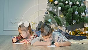 Children write letters to Santa Claus. To children it is cheerful. Little boy and girl lie on a floor near Christmas