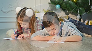 Children write letters to Santa Claus. To children it is cheerful. Little boy and girl lie on a floor near Christmas