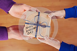 Childrens hands and daddy hands holding a gift or present box with kraft paper and tied blue ribbon tag on Happy fathers day