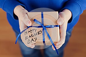 Childrens hands holding a gift or present box with kraft paper and tied blue ribbon tag on Happy fathers day