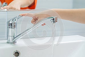 The childs hand closes the water from the mixer by pressing the finger on the handle