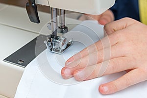 A childs hand pulling a white textil throught a sewing machine photo