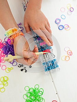 childs hands with band loom, croche hook and multicoloured elastic bands