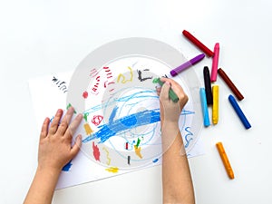 Childs hands drawing with colorful wax crayons on white paper, top view. Creative art concept for educational and