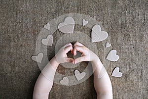 Childs hands in heart shape gesture and cardboard handmade hearts on canvas burlap background. Valentine day, womans day, love,