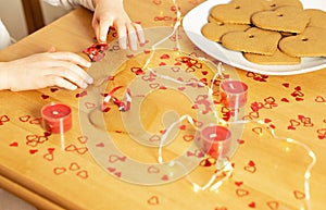 Childs hands making garland from the homemade heart cookies on the background of the many red hearts