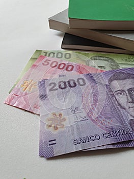 Chilean banknotes and stacked books on white background