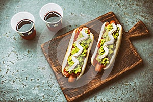 Chilean Completo Italiano. Hot dog sandwiches with tomato, avocado and mayonnaise served on wooden board with drink in photo