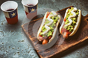 Chilean Completo Italiano. Hot dog sandwiches with tomato, avocado and mayonnaise served on wooden board with drink in photo