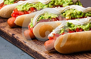 Chilean Completo Italiano. Hot dog sandwiches with tomato, avocado and mayonnaise on wooden board. closeup photo