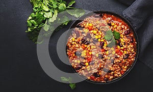 Chili con carne with beef, red beans, paprika, corn and hot peppers in tomato sauce, spicy tex-mex dish in a cooking pot, black