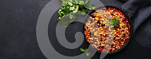 Chili con carne with beef, red beans, paprika, corn and hot peppers in tomato sauce, spicy tex-mex dish in a cooking pot, black