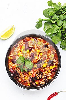 Chili con carne with beef, red beans, paprika, corn and hot peppers in tomato sauce, spicy tex-mex dish, white table background,