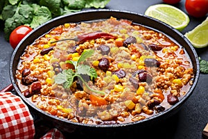 Chili con carne with beef, red beans, paprika, sweet corn and hot peppers in tomato sauce, spicy tex-mex dish in frying pan, black