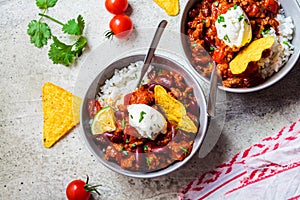 Chili con carne with rice, sour cream and nachos in gray bowl. Beef stew with beans, tomato sauce,  sour cream and rice.