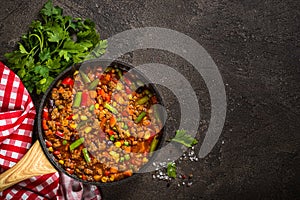 Chili con carne in skillet on dark stone table.