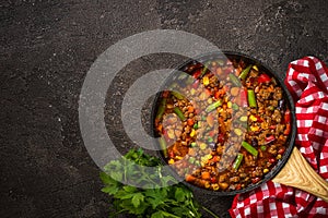 Chili con carne in skillet on dark stone table.