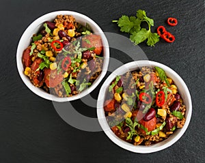 Chili con carne in a white ceramic bowl on black stone background. Cooked with ground beef, tomatoes, peppers, beans, corn, garlic