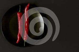 Chili pepper on a plate on a black background. Minimalism.