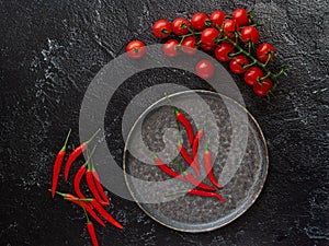 Chili peppers on a plate, next to cherry tomatoes and chilly peppers on a black background. View from above