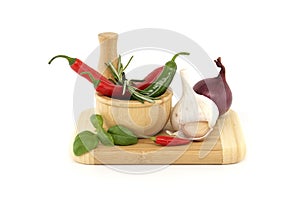 Chili peppers in wooden mortar and herbs over white