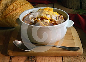Chili in white crock with onions and cheddar cheese on rustic wood table photo
