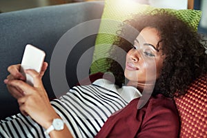 This chill time was much needed. a young woman using a mobile phone while relaxing on the sofa at home.