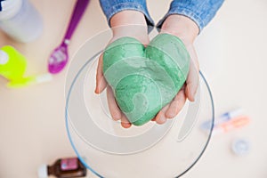 Chilld`s hands holding green slime in heart shape. photo