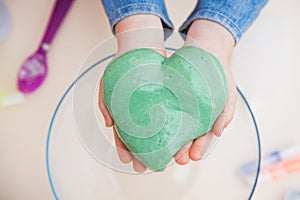 Chilld`s hands holding green slime in heart shape. photo