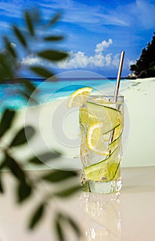 Chilled cocktail with lemon and ice on the background of the beach, blue sea and blue sky