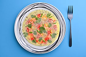 Chilled cucumber avocado soup with salmon fish, tomato, pepper, fresh greenery served in a plate over blue background.