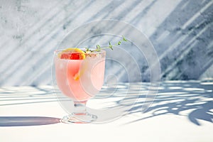 A chilled drink with grapefruit or red orange in glasses on a gray background under the shadow of palm leaves. Summer