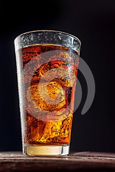 Chilled glass of cola drink with ice cubes isolated on dark background