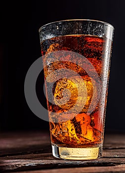 Chilled glass of cola drink with ice cubes isolated on dark background